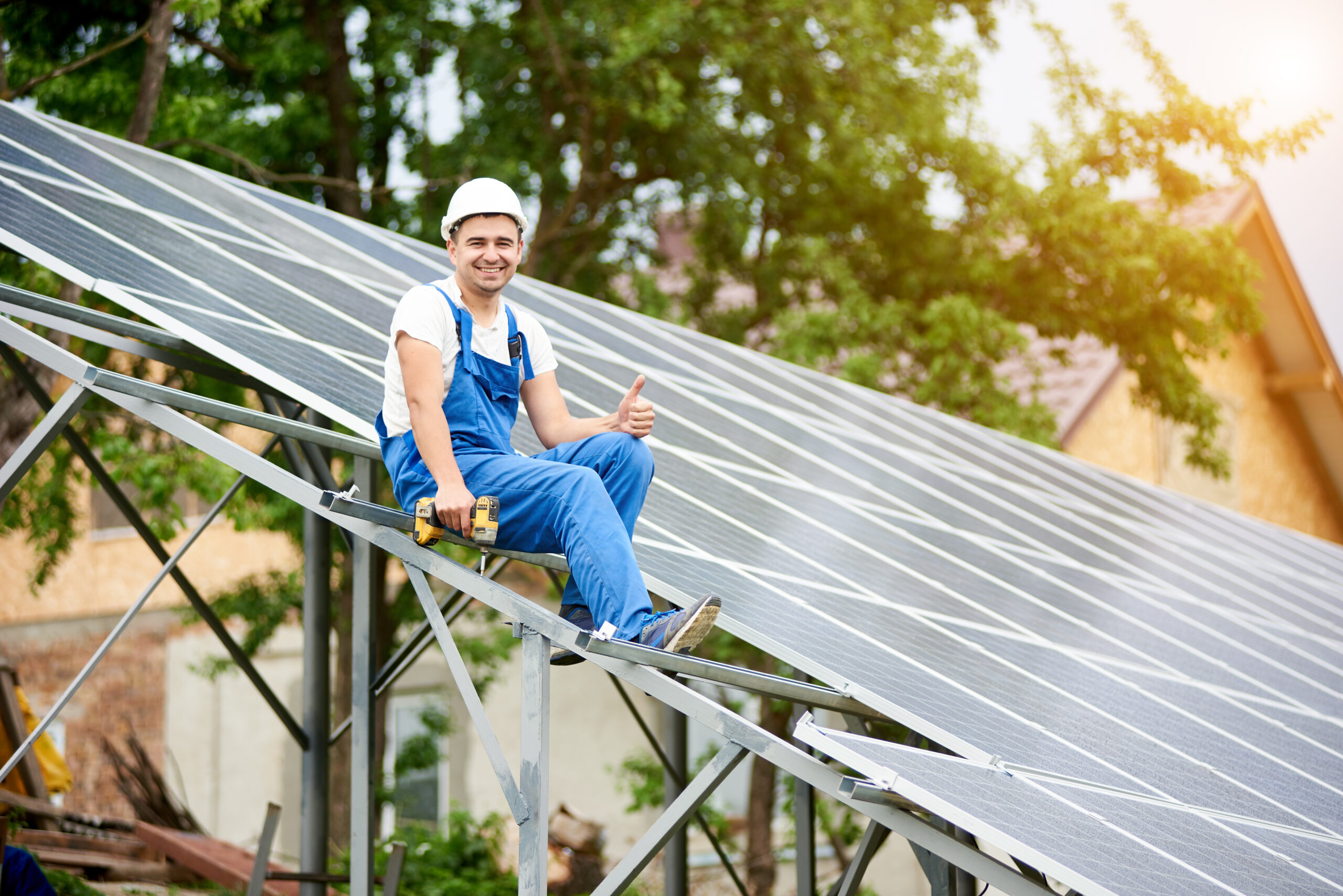 Lächelnder Monteur von Photovoltaikanlagen, der auf einer am Boden montierten Solaranlage sitzt.